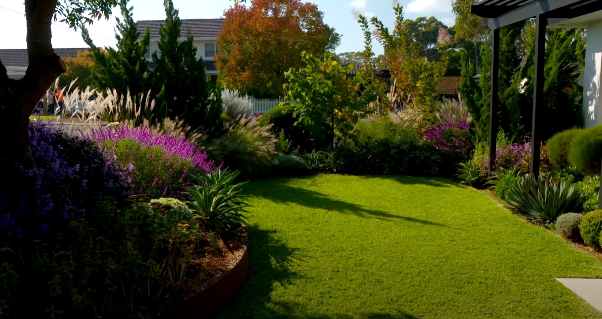 Beautifully maintained backyard with perfect lawn, colorful perennial borders, and mature trees providing natural shade