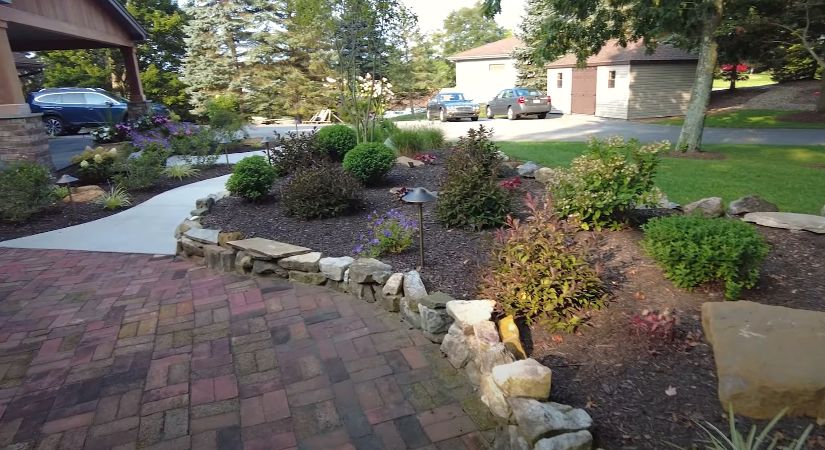 Professional landscaping services showing curved pathways, stone retaining walls, and carefully planned garden beds with colorful flowers and shrubs